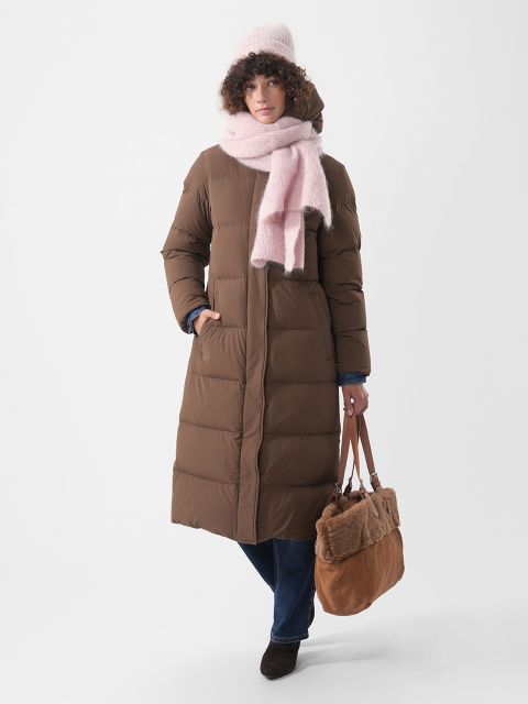 Eine Person trägt einen langen braunen Daunenmantel, eine rosa Mütze und einen rosa Schal und hat eine braune Tragetasche dabei.